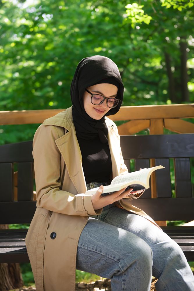 Woman in headscarf calmly reading in a wooded park