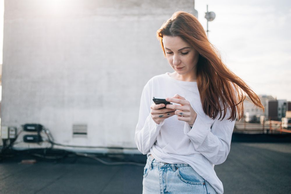 Red haired woman texting on roof