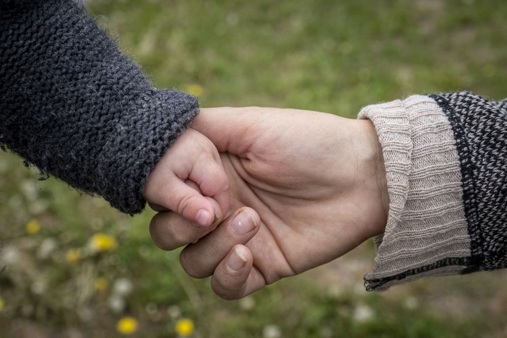 Baby’s hands in mother’s hand in front of grass