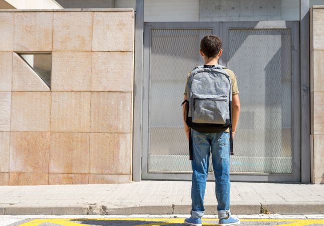 Back of child in backpack standing in front of the school doors