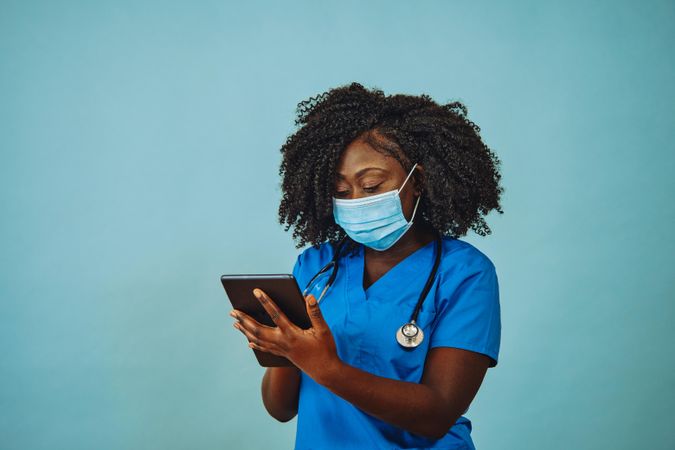 Portrait of serious Black medical professional in face mask dressed in scrubs with tablet