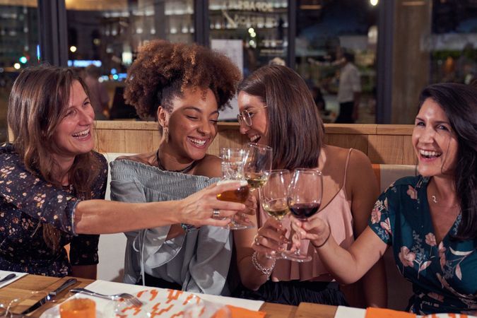 Multiracial women clinking wineglasses in restaurant