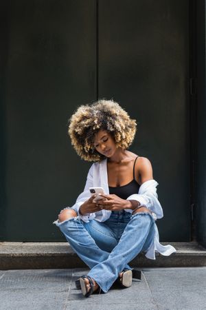 Black woman using smartphone while sitting on concrete border