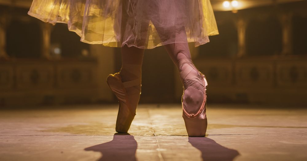 Close Up of Ballerina Feet in Pointe Shoes and Tutu Dancing Gracefully on Theatre Stage with Dramatic Lighting.