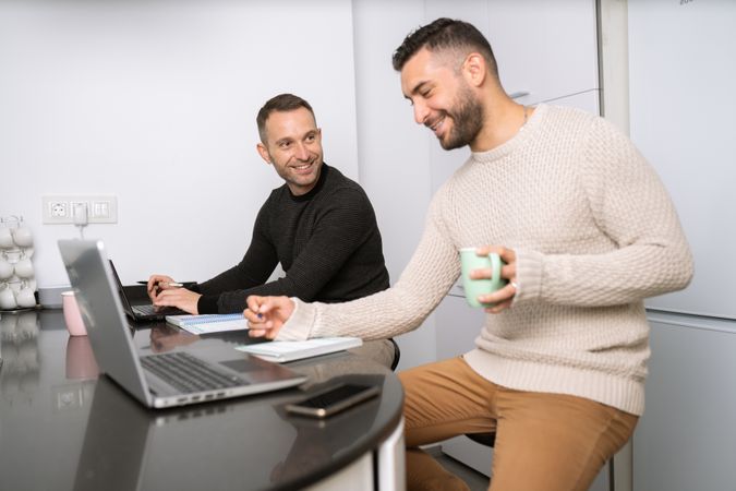 Two men sitting at kitchen counter happily working from home