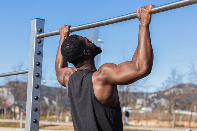 Unrecognizable strong Black sportsman working out on bar in town