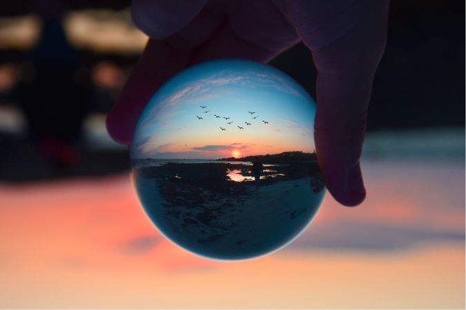 Person holding clear glass ball on the beach during sunset