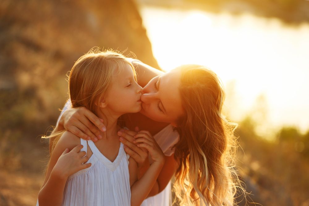 Woman leaning down giving her daughter a kiss at dusk