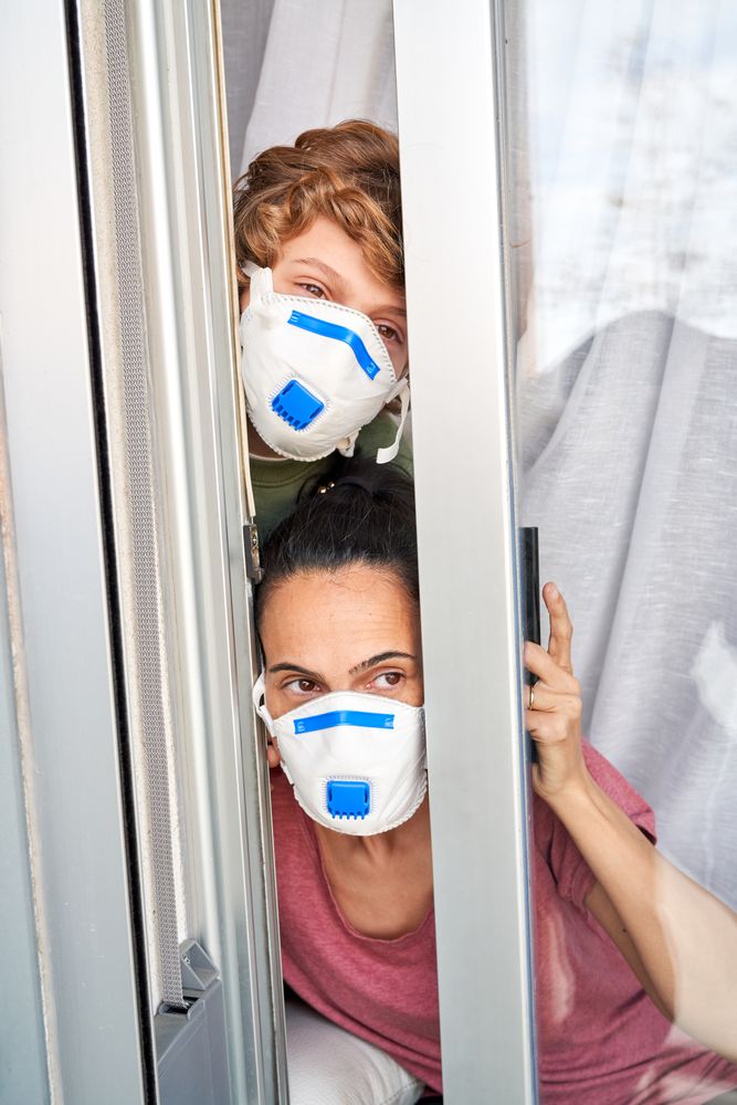 Mother with son in protective masks looking out window