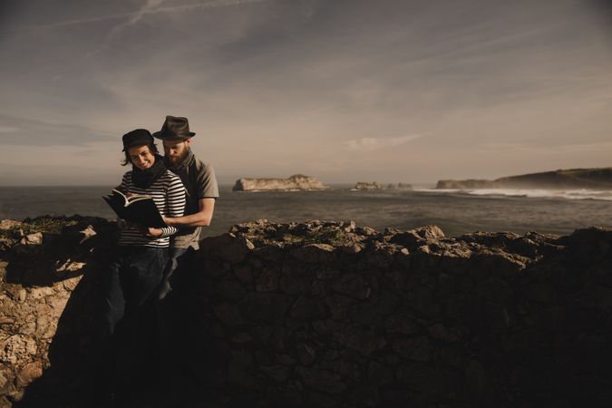 Man near woman with books near stones on shore