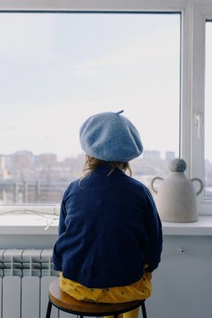 Back view of girl wearing blue beret sitting on chair looking at the window