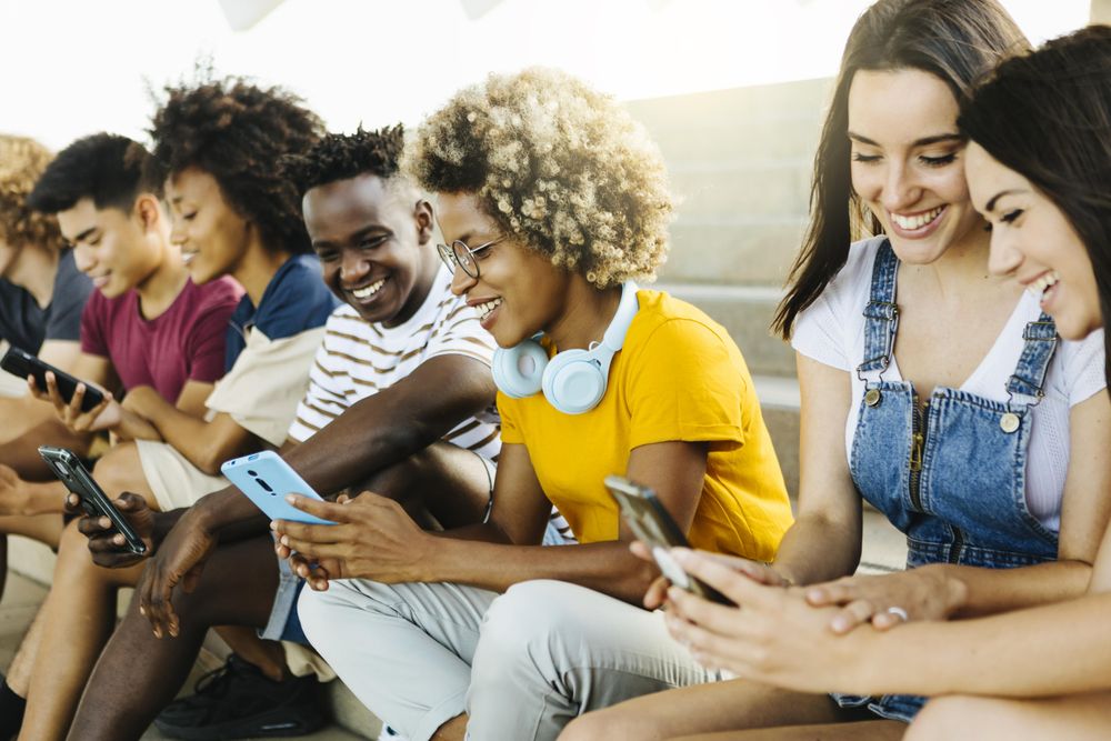 Multiethnic group of young adults using mobile phone while sitting on city stairs