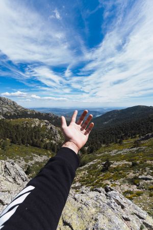 Person stretching hand to blue sky above mountain valley