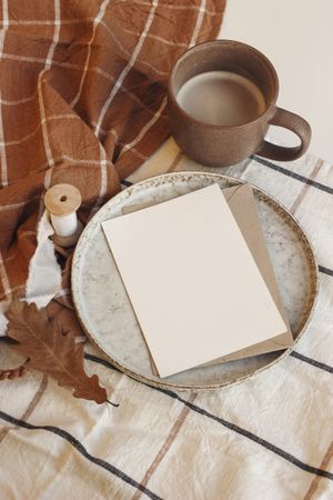 Blank card on ceramic plate on autumn themed table setting with cup of coffee
