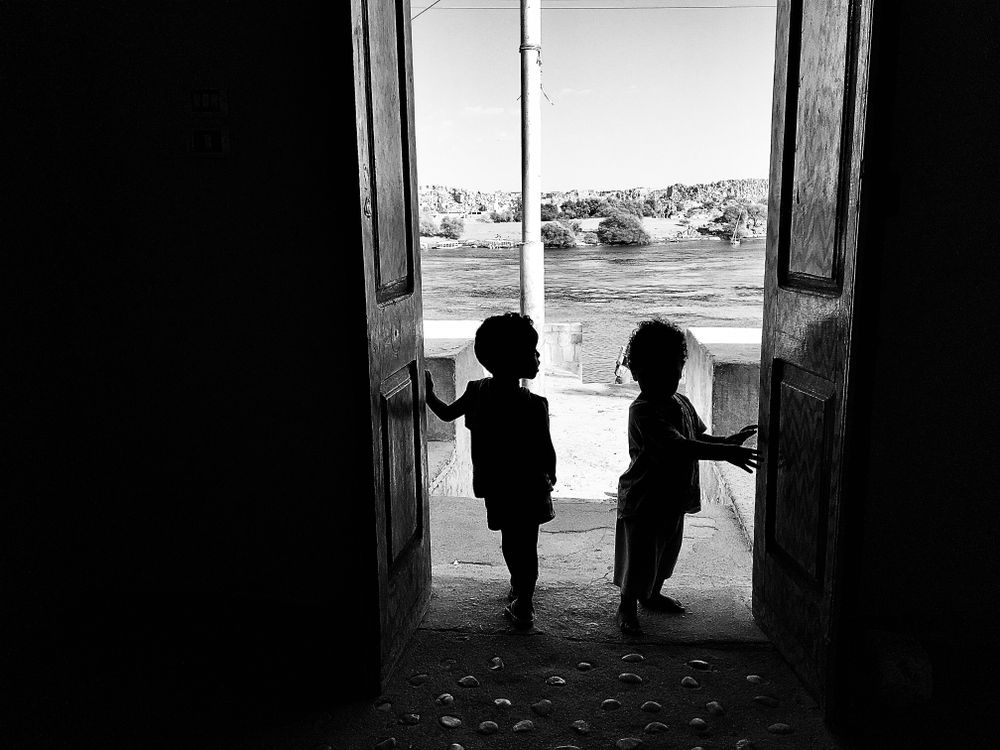 Grayscale photo of two children standing at the door in Aswan, Egypt