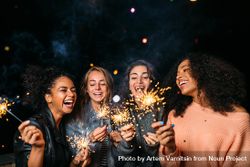 Multi-ethnic group of laughing women celebrating with sparklers 56yZL0