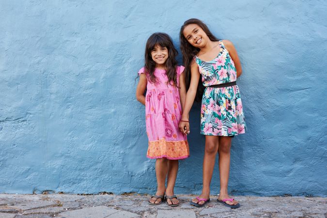 Full length portrait of two little beautiful girls standing together against blue wall