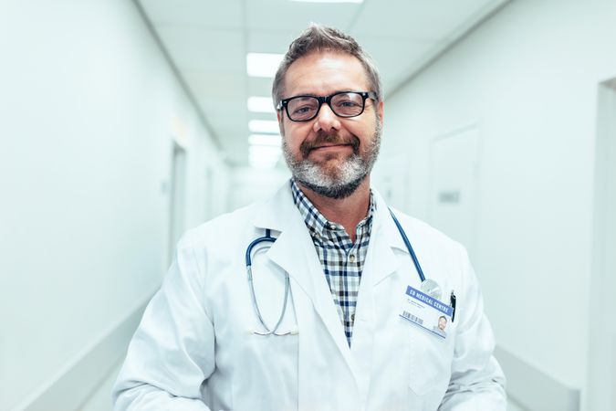 Portrait of happy mature male doctor standing in hospital corridor