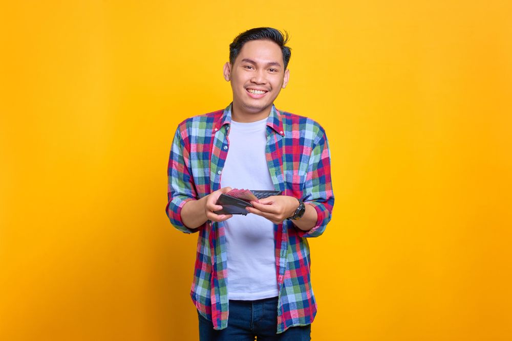 Content Asian man smiling while taking cash out of his wallet