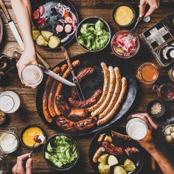 German sausages and pretzels displayed on wooden table with hands holding beer and serving food