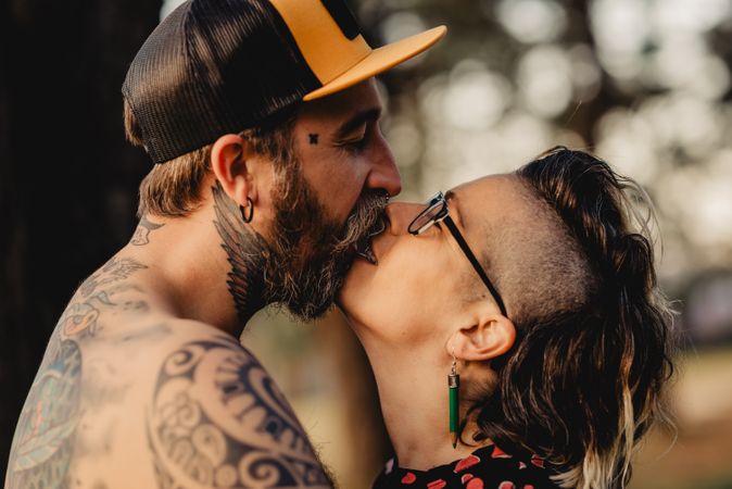 Happy couple hugging and kissing near tree in park