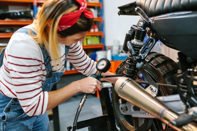 Mechanic woman checking tire air pressure of motorcycle