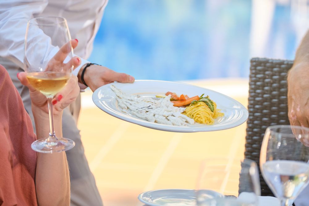 Crop waiter bringing dish to customers