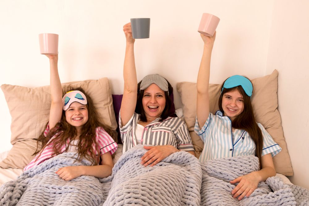 Mother and daughters celebrating with raised mugs in bed.