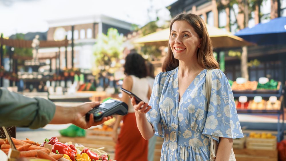 Woman Using Smartphone with Contactless NFC Payment Technology to Buy Organic Vegetables at a Farmers Market.