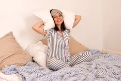 Woman smiling, holding pillows, sitting in cozy bed.