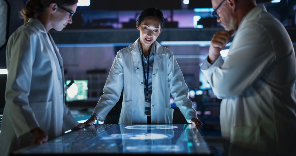 Modern Hospital Medical Research Center: Diverse Colleagues Gathered Around Interactive Touch Screen Table With MRI Scans Of Brain On Display.