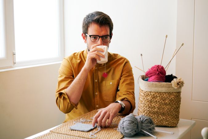 Man drinking hot tea during knitting