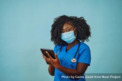 Portrait of Black medical professional in face mask dressed in scrubs holding tablet 5zNzn5