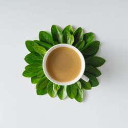 Morning coffee and green leaves in flower shape on light background