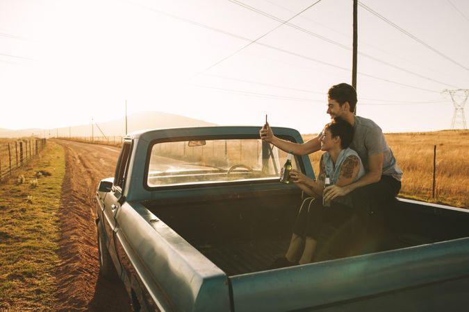 Couple taking selfie using mobile phone sitting in back of classic truck