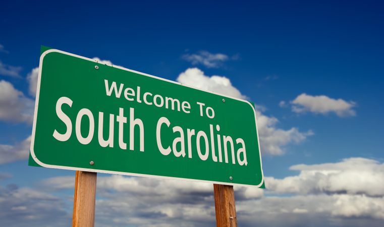 Welcome To South Carolina Green Road Sign Over Blue Sky with Some Clouds.