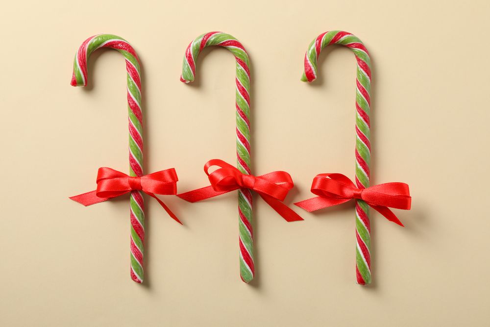 Sweet candy canes with bow on color background. Flat lay