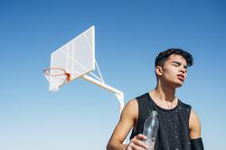 Young man playing on basketball court outdoor drinking water