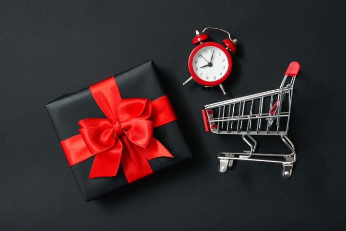 Gift box, alarm clock and shop trolley on dark background