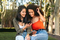 two young women sitting watching something on the cell phone