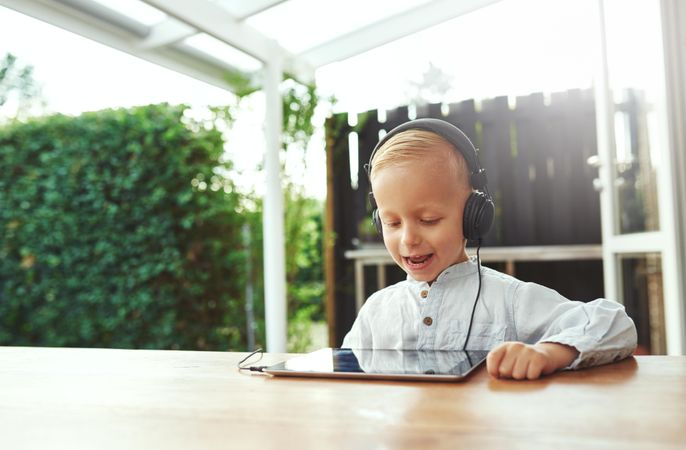 Happy blond boy using headphones listening to something on digital tablet, copy space
