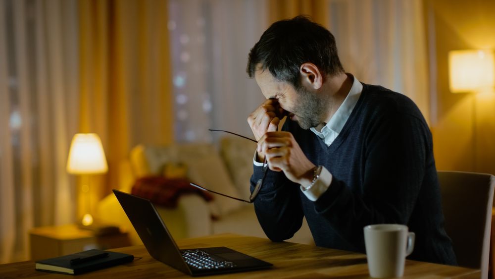 Tired  Man Works on a Laptop. He's Eyes Fatigued, He Temporarily Takes off His Glasses and Rubs His Eyes.