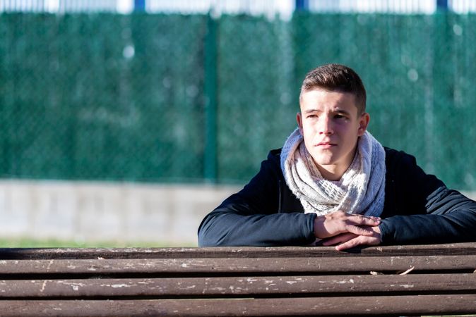 Teenage male sitting behind a wooden bench in a city park in contemplation