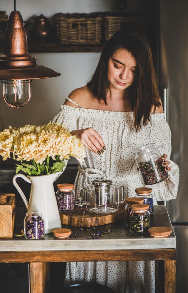 Woman in rustic kitchen putting loose tea leaves into tea pot