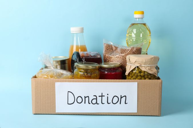 Donation box with different food on blue background. Volunteering