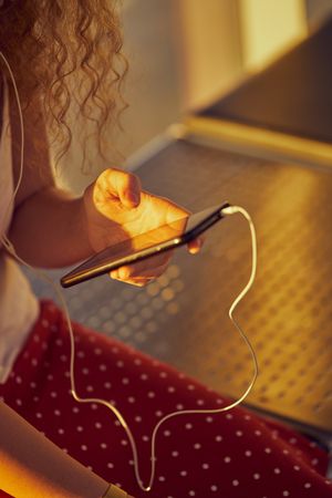 anonymous woman sitting on metal bench with earphones and smartphone