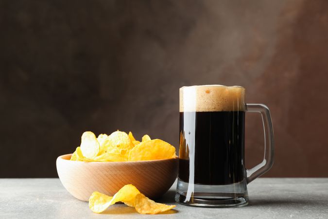 Glass of dark beer and chips on grey table, space for text