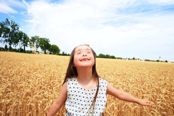 Happy girl with Down syndrome looking up at the sky in a wheat field