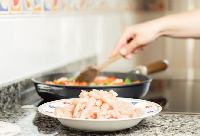 Raw chiken dish and female cooking in a pan
