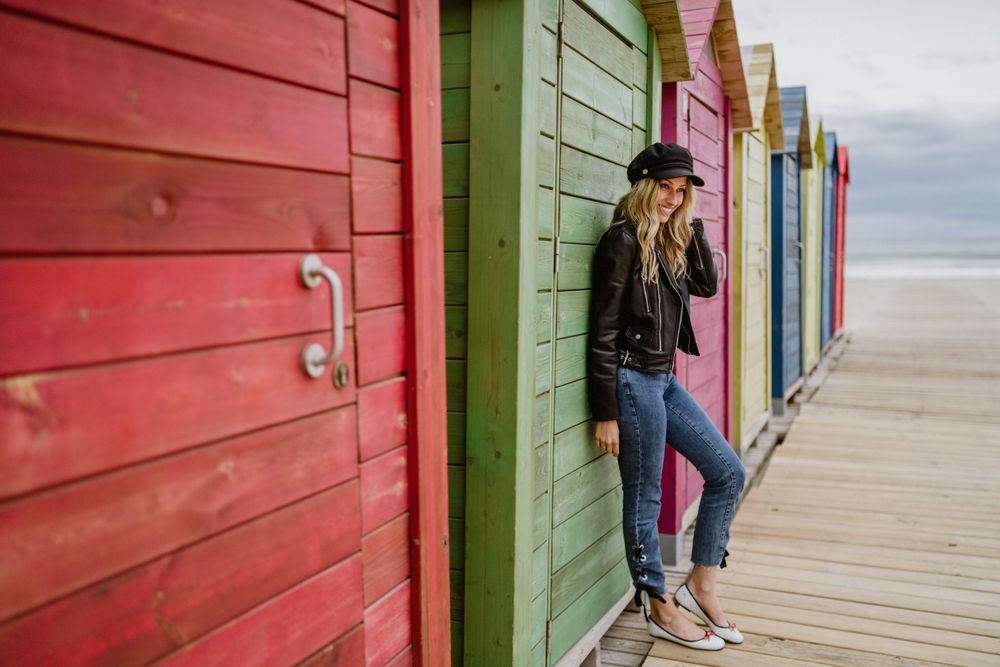 Stylish woman smiling and leaning on bright wooden cabins on beach